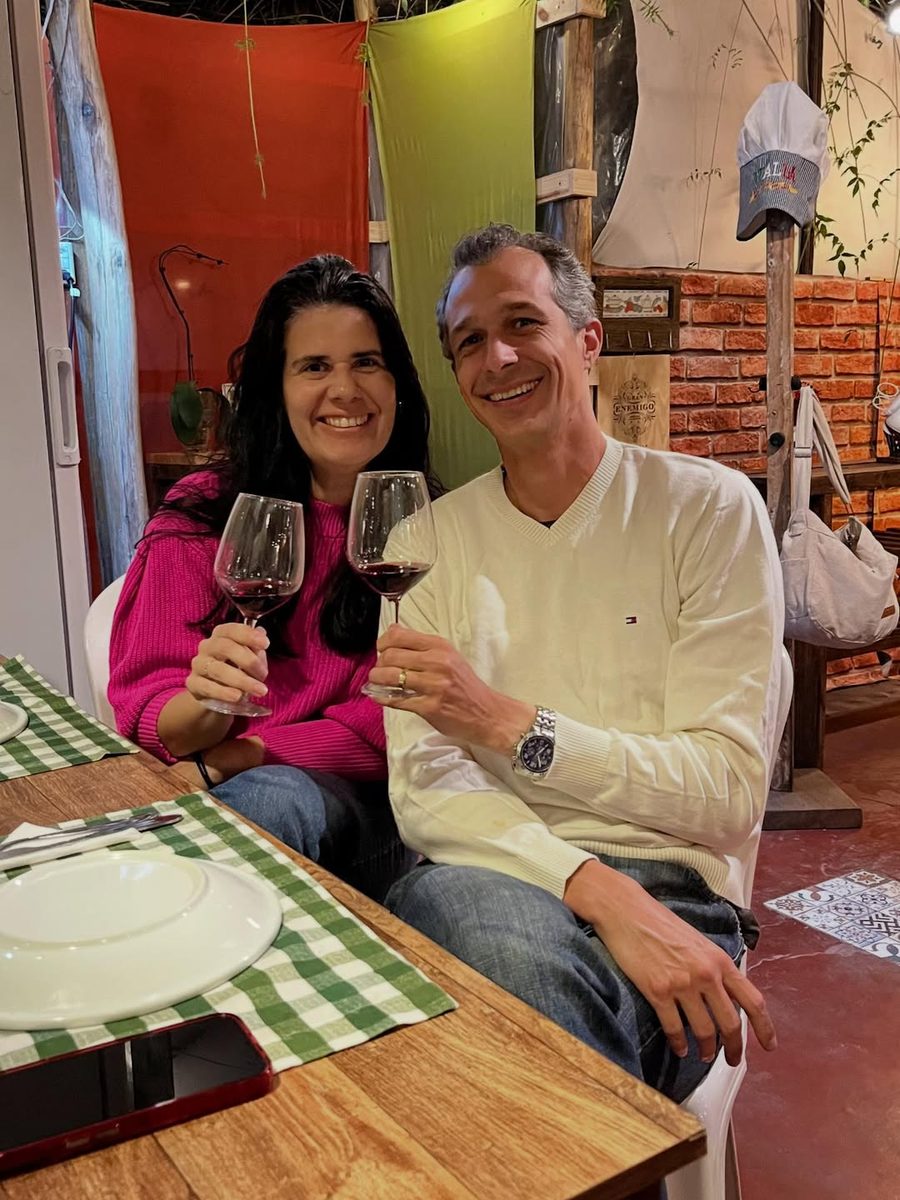 Paulo e Paty, sommeliers e curadores da Divine Wine, brindando com taças de vinho tinto